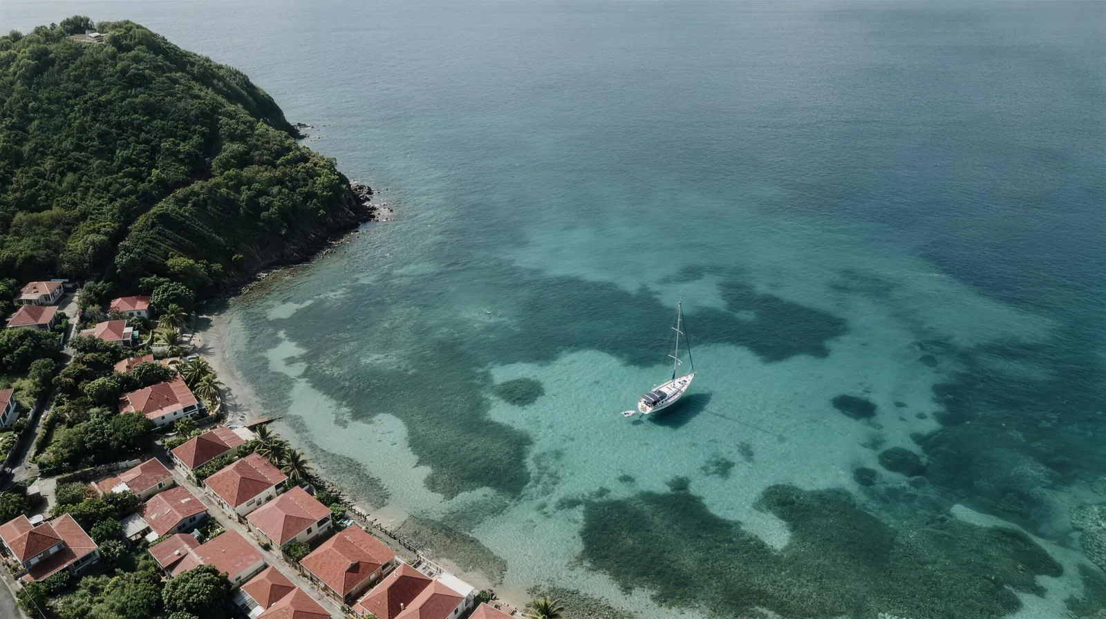 Aerial view of a sloop lying to its anchor over sand and seagrass in a bay at Les Saintes.