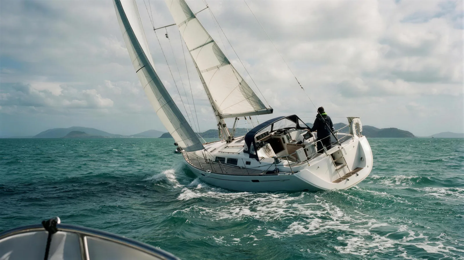 SV Barefoot heeled on a beam reach under full sail, the helm distant, open water beyond.